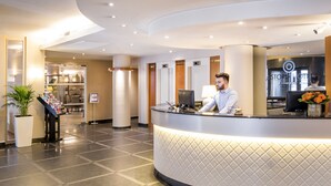 Zona de recepción de un hotel con mostrador curvo, una recepcionista, un ordenador portátil y el cartel del hotel a la vista.