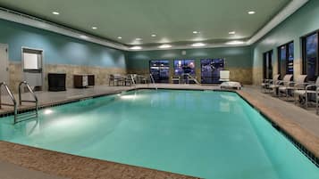 Una gran piscina interior con suelo de baldosas, rodeada de sillas y un banco.