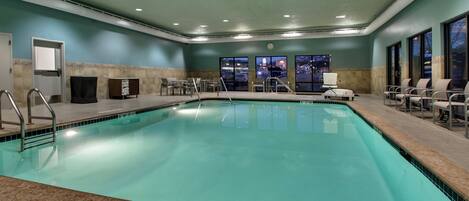 Una gran piscina interior con suelo de baldosas, rodeada de sillas y un banco.