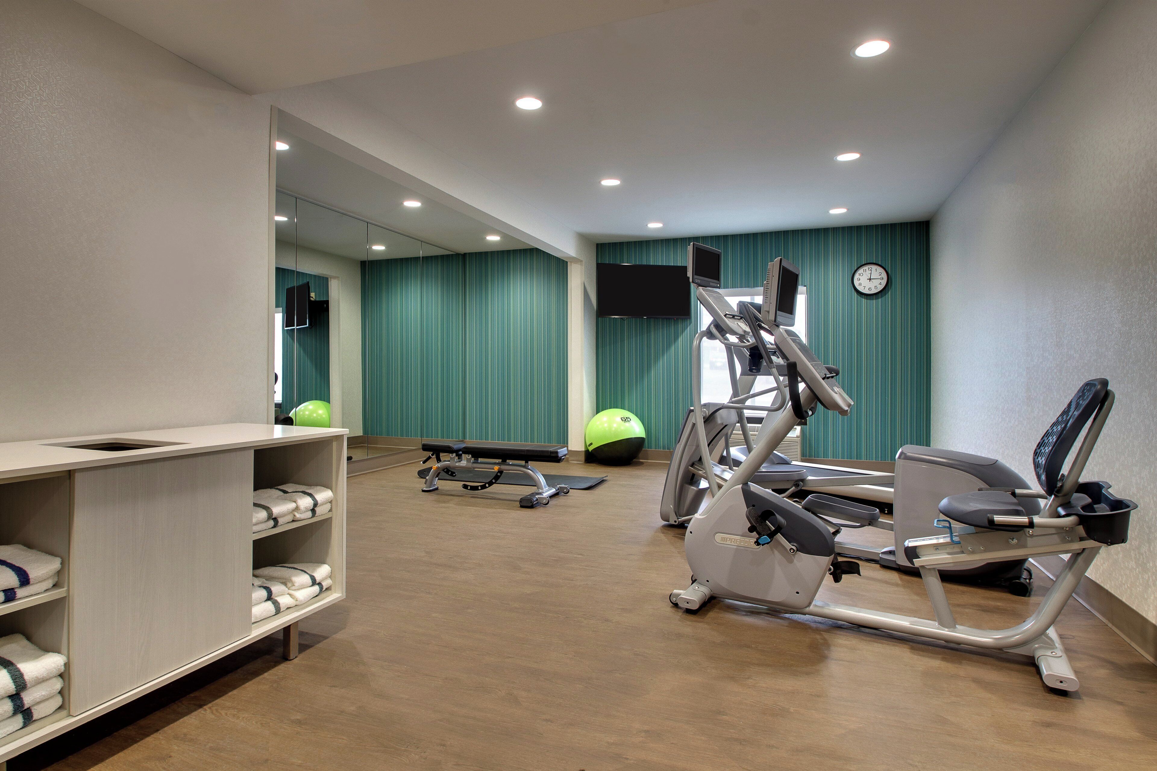 A gym with exercise equipment, a mirror, a television, and a clock on the wall.