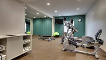 A gym with exercise equipment, a mirror, a television, and a clock on the wall.