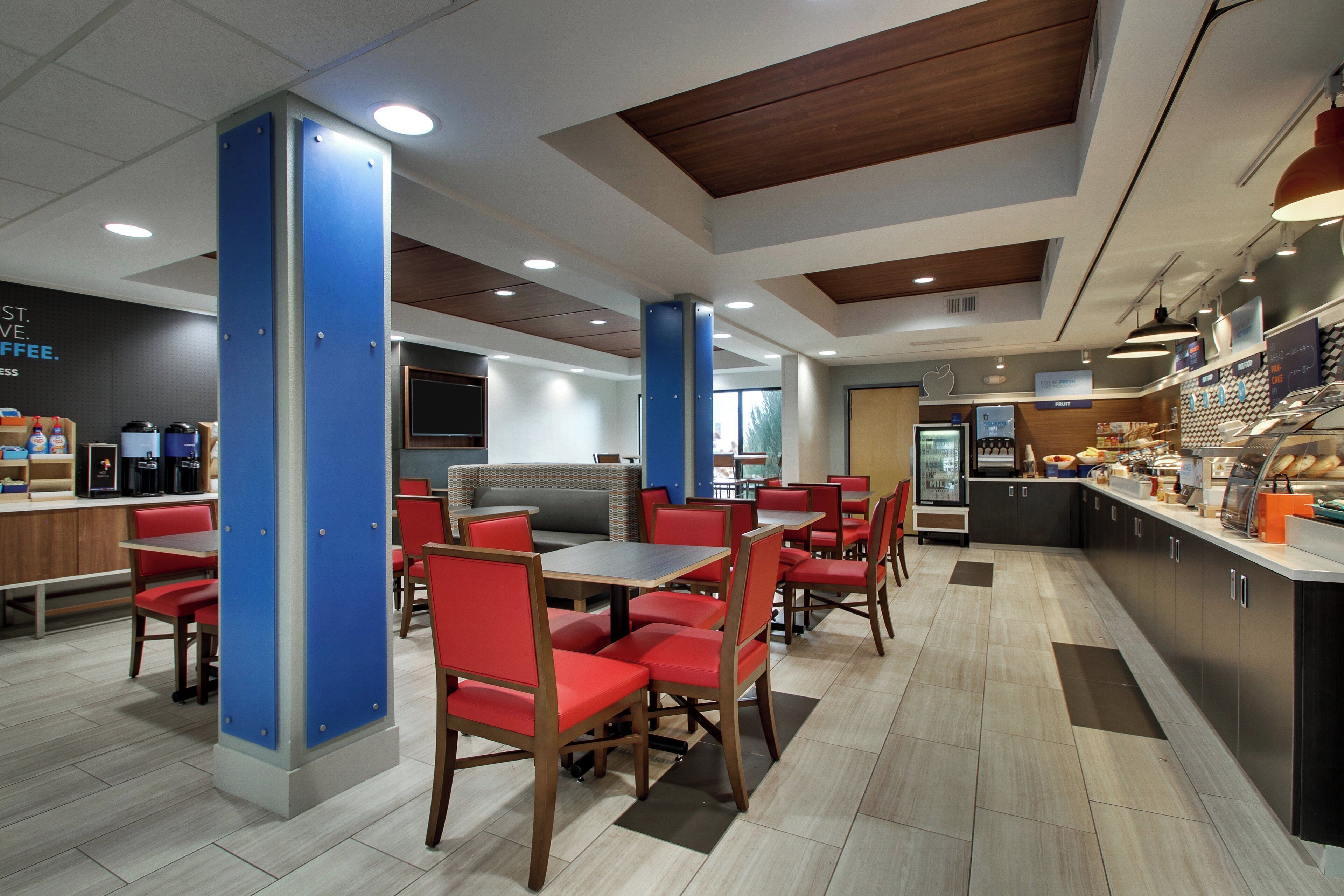 A modern cafe with seating arrangements, a counter with food items, and a refrigerator.