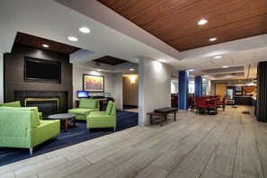 A hotel lobby with seating areas, a flat-screen TV, a fireplace, and a dining area. - Holiday Inn Express & Suites - Interstate 380 at 33rd Avenue by IHG (Cedar Rapids)