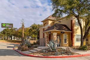 Un hotel con fachada amarilla, el número 1015, y un jardín delantero ajardinado con plantas de agave.