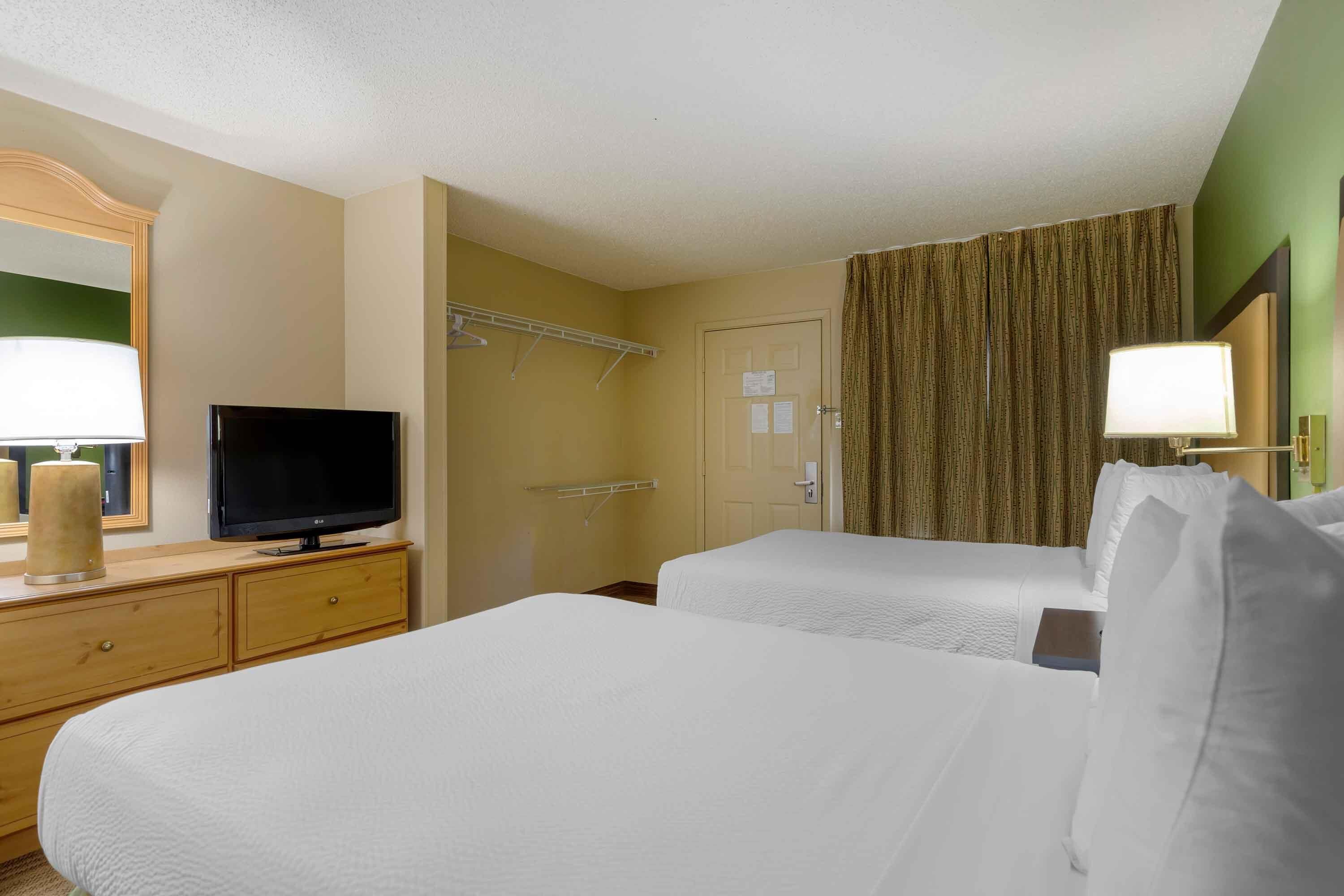 Habitación de hotel con dos camas, un televisor en una cómoda, un espejo y una ventana con cortinas.