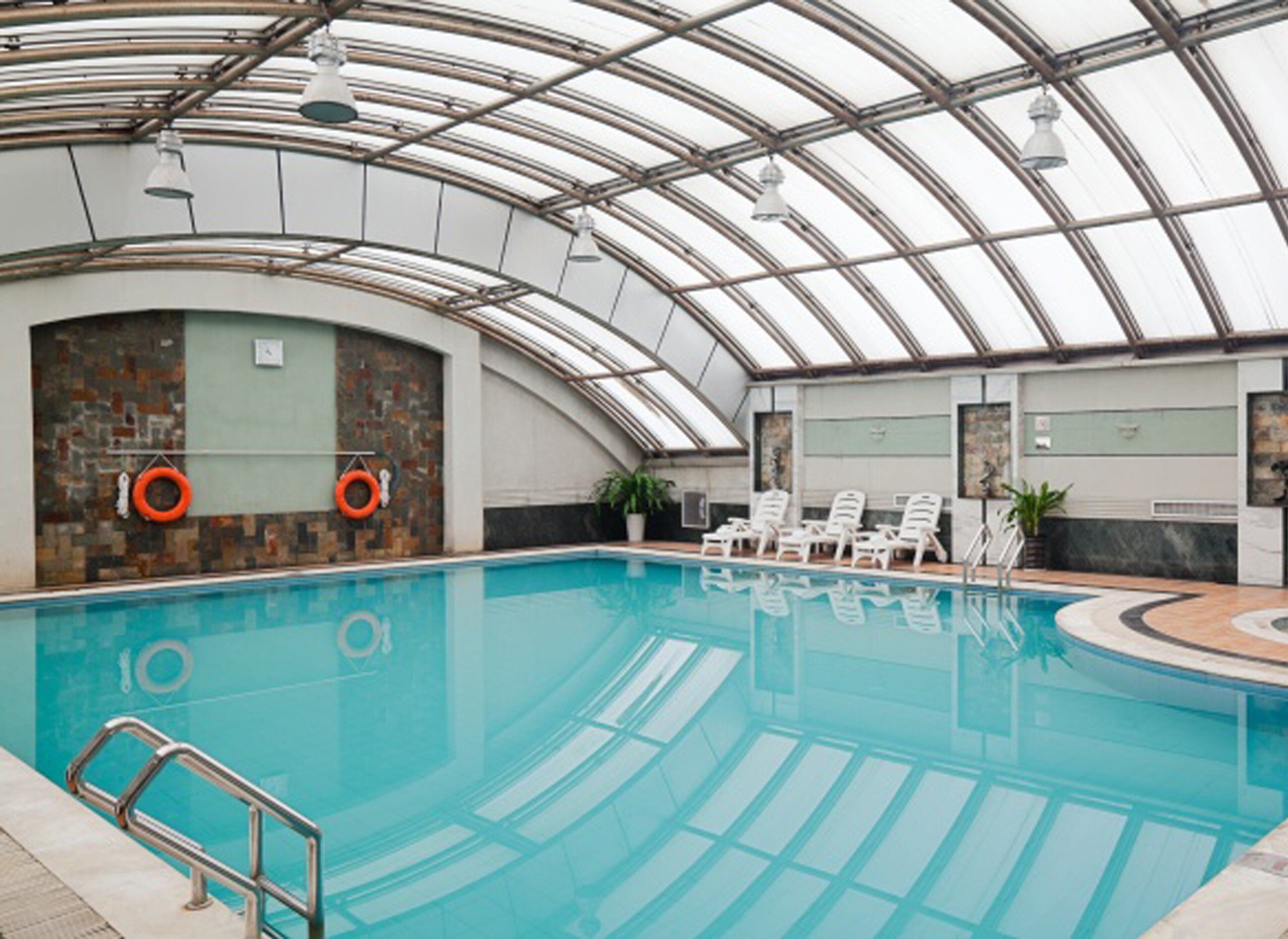An indoor swimming pool with a glass ceiling, a lifebuoy, and a lounge area with chairs.