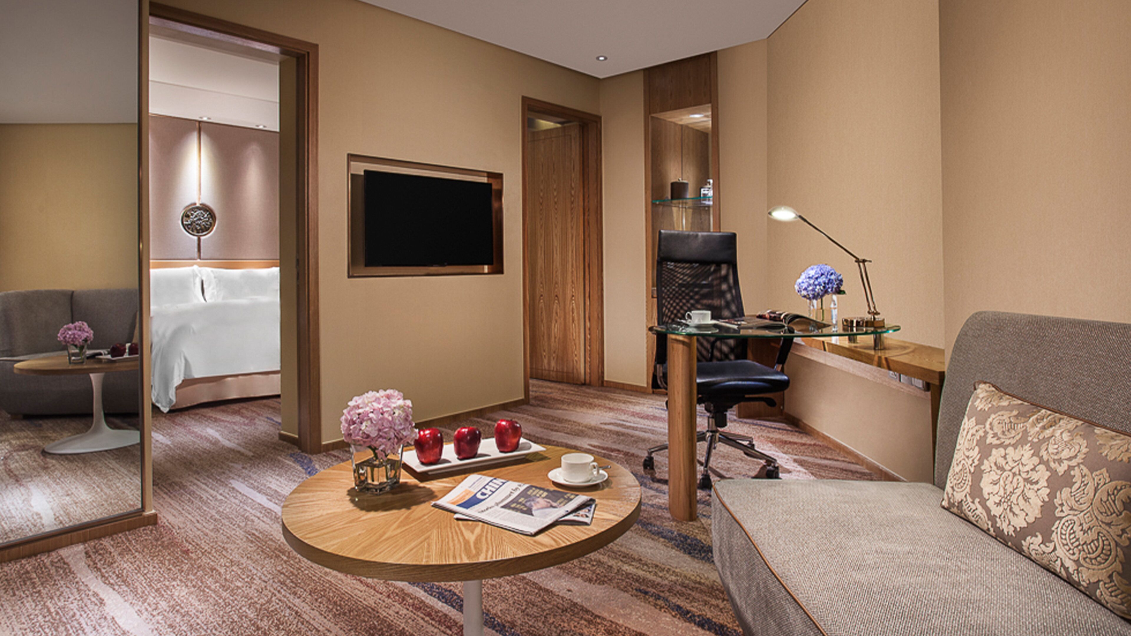 Une chambre d’hôtel avec un canapé, une petite table ronde sur laquelle sont posés des magazines, un bureau avec une chaise, une télévision et un lit.