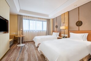 A hotel room with two beds, a television, a small table, and a window with curtains.