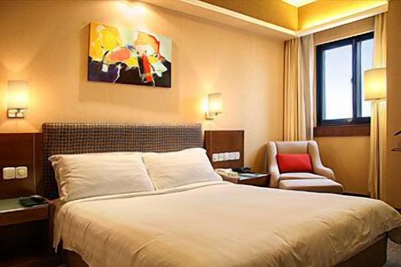 A hotel room with a large bed, a headboard, a painting on the wall, a chair, and a window with curtains.