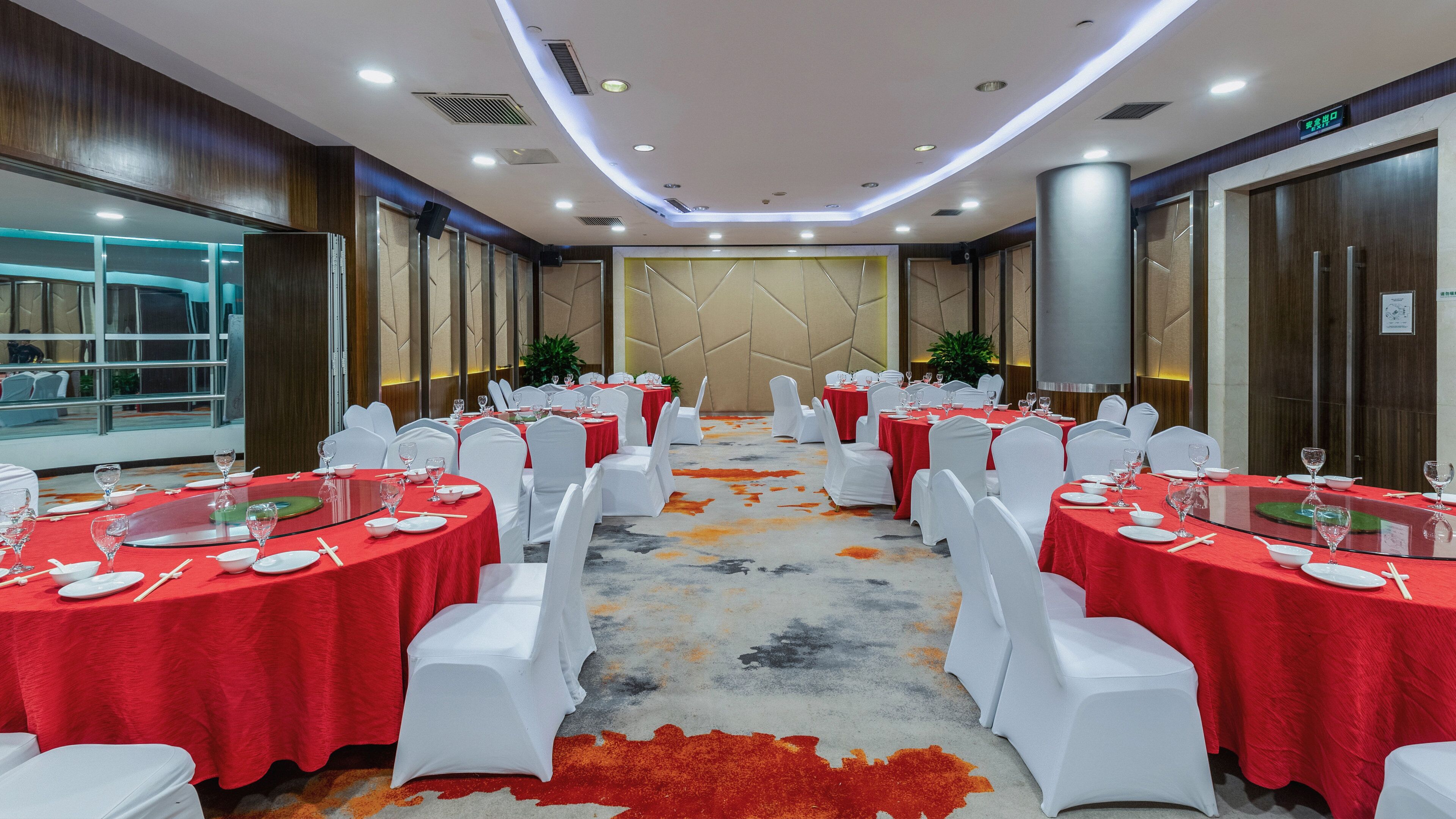 A conference room with round tables, white chairs, and red tablecloths.