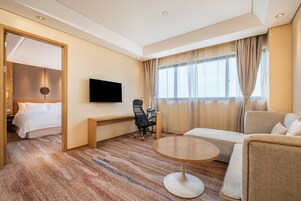 Habitación de hotel con cama, escritorio, televisor, sofá y ventana con cortinas.