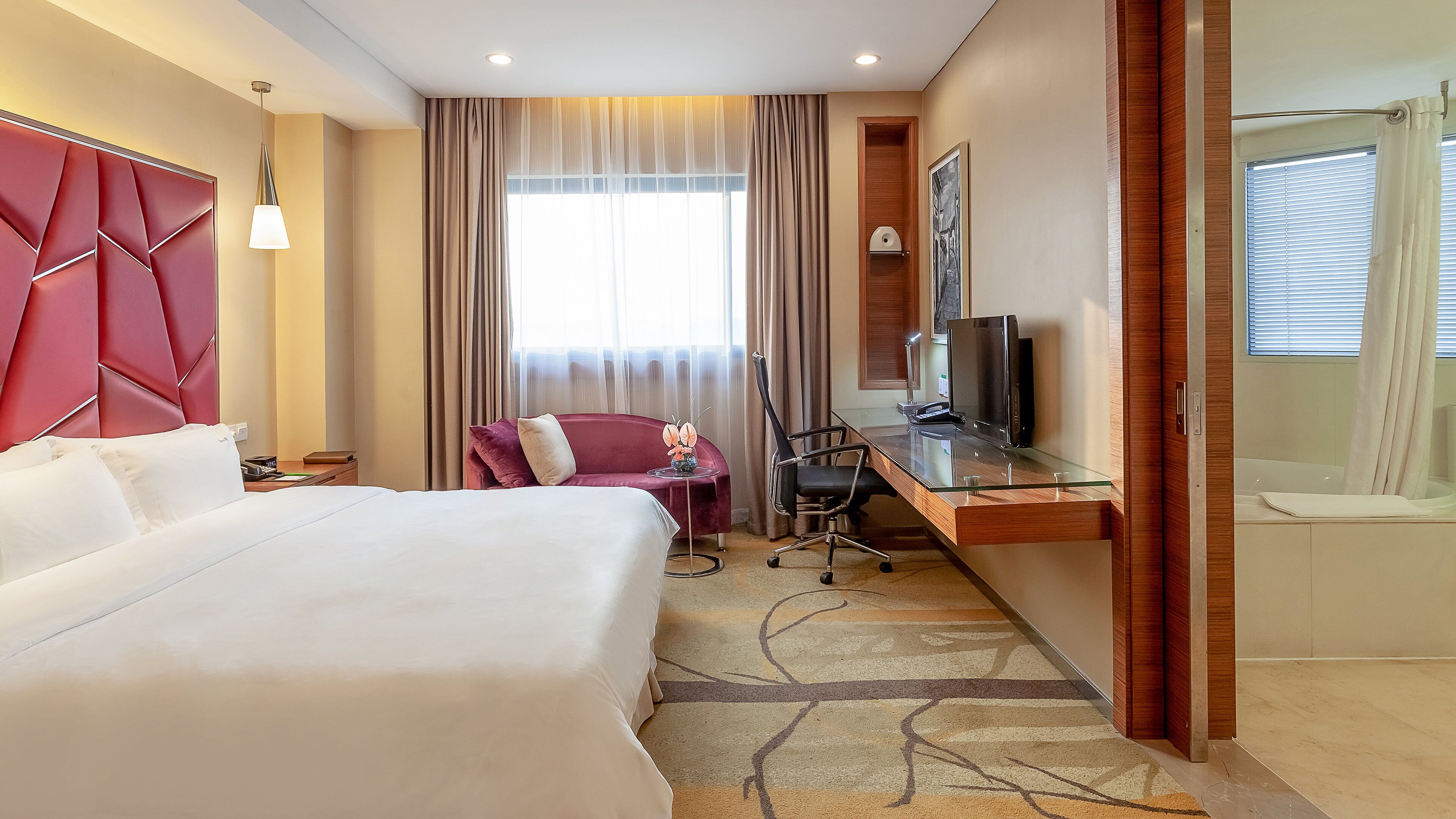 A hotel room with a large bed, a desk with a computer, a chair, and a television.