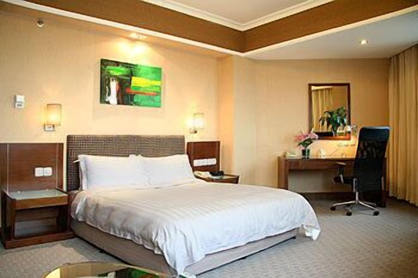 A hotel room with a large bed, a desk with a chair, a mirror, and a painting on the wall.