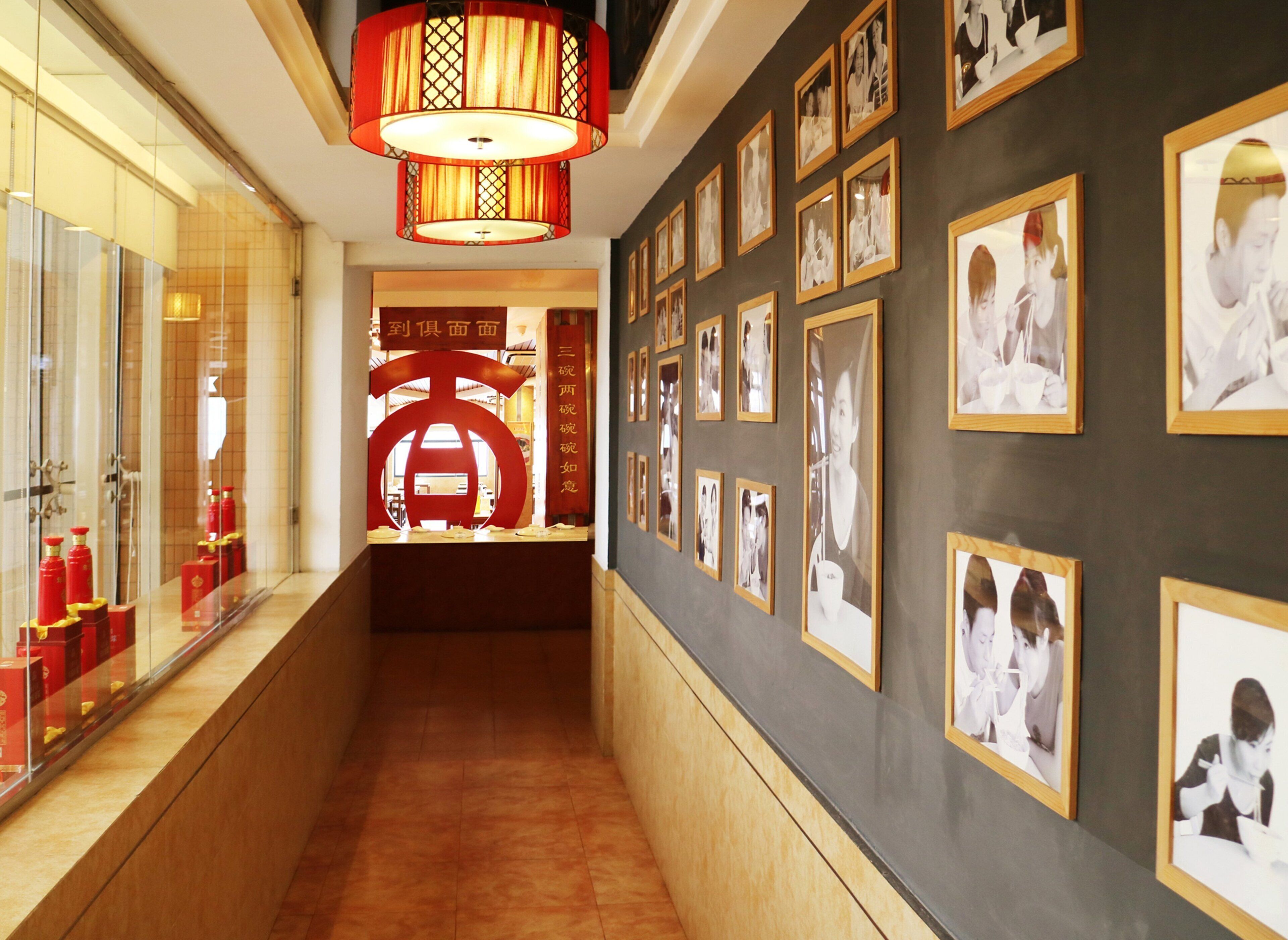 Un pasillo con fotografías enmarcadas en las paredes, un letrero decorativo rojo y una lámpara colgante de estilo tradicional.