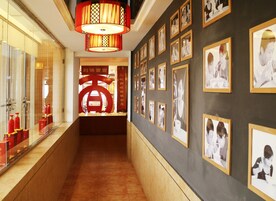 Un pasillo con fotografías enmarcadas en las paredes, un letrero decorativo rojo y una lámpara colgante de estilo tradicional.