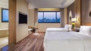 Une chambre d’hôtel avec deux lits, une télévision, un bureau et une vue sur le paysage urbain.