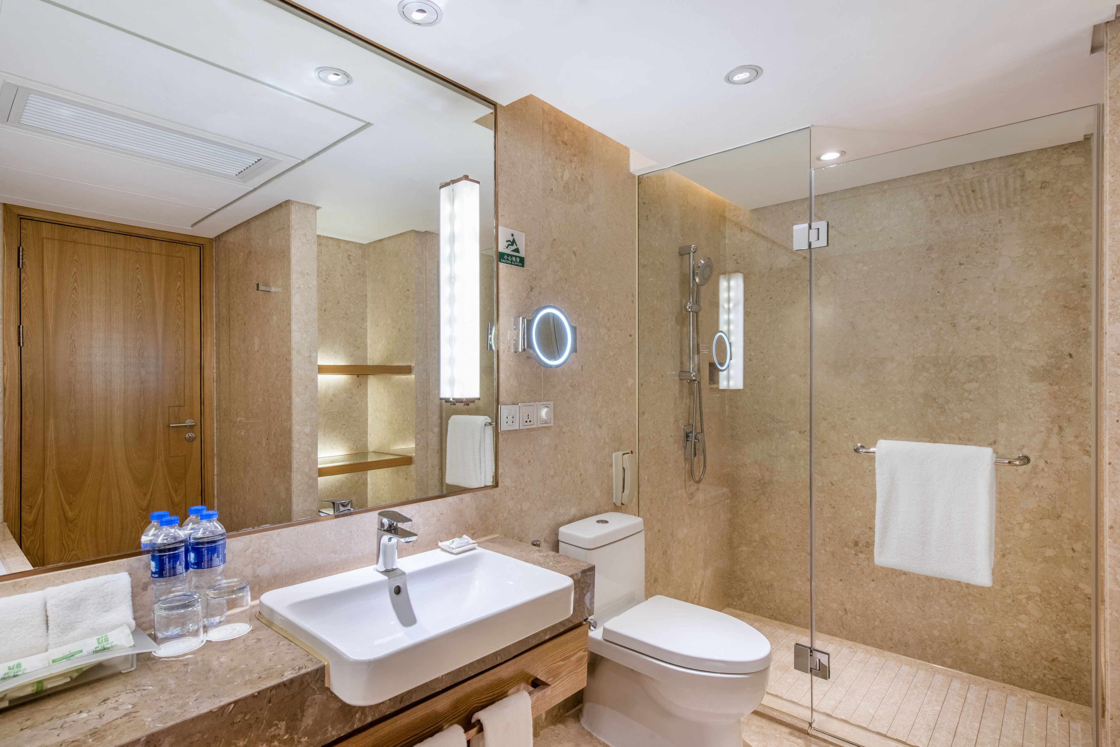 A modern bathroom with a large mirror, a sink, a toilet, and a glass-enclosed shower.