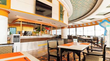 Um amplo saguão de hotel com teto curvo, balcão de recepção central e diversas mesas de jantar com cadeiras.