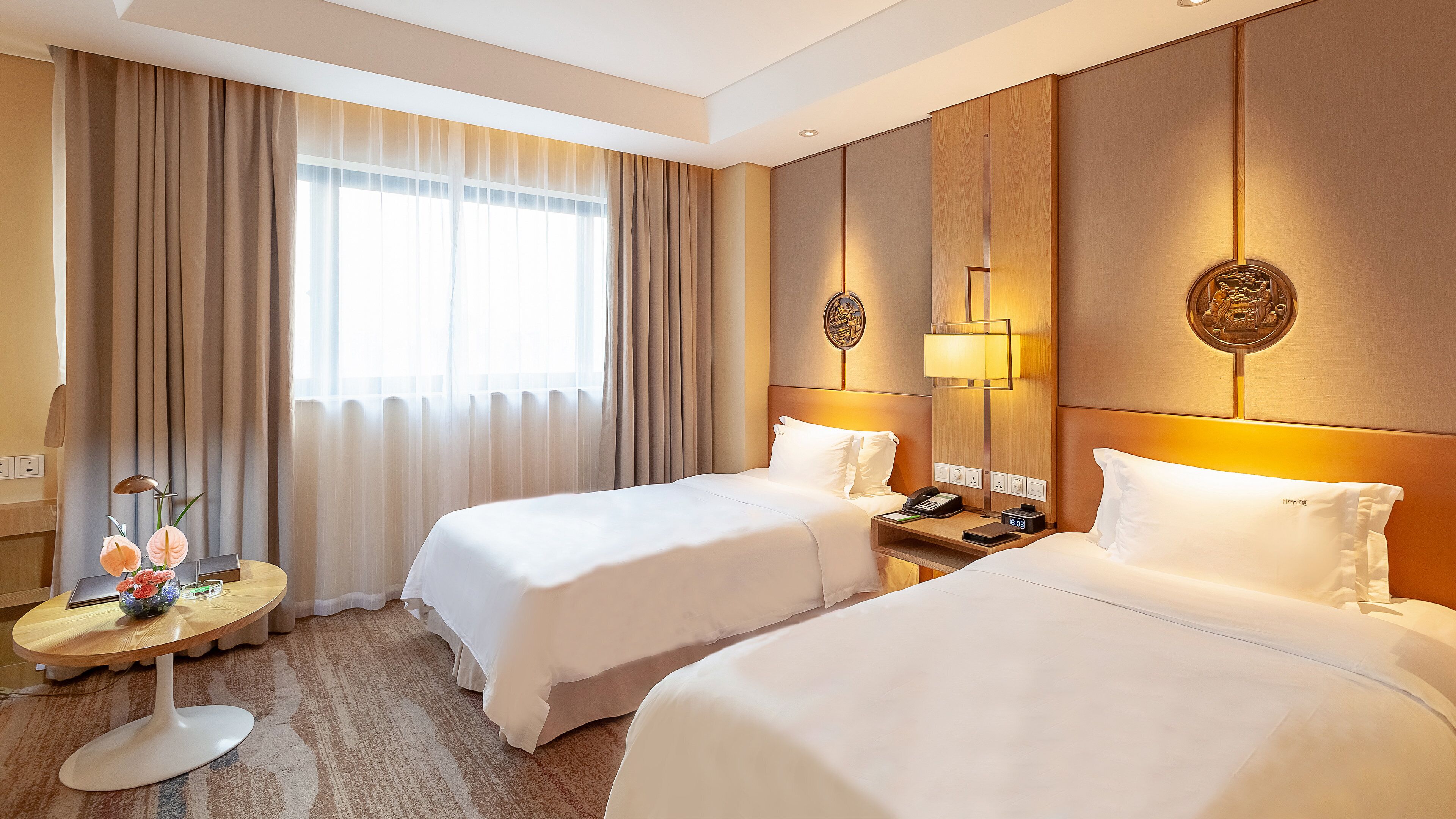 Hotellihuone, jossa on kaksi sänkyä, yöpöytä lampun, kellon ja koriste-esineen kanssa.