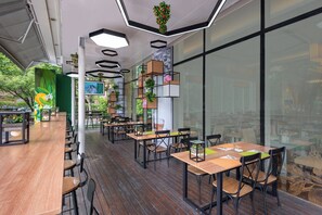 Ein modernes Café-Interieur mit Holztischen und -stühlen, geometrischen Deckenleuchten und Topfpflanzen.