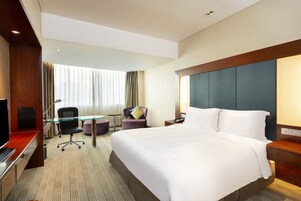 A hotel room with a large bed, a desk, a chair, a TV, and a window with curtains.