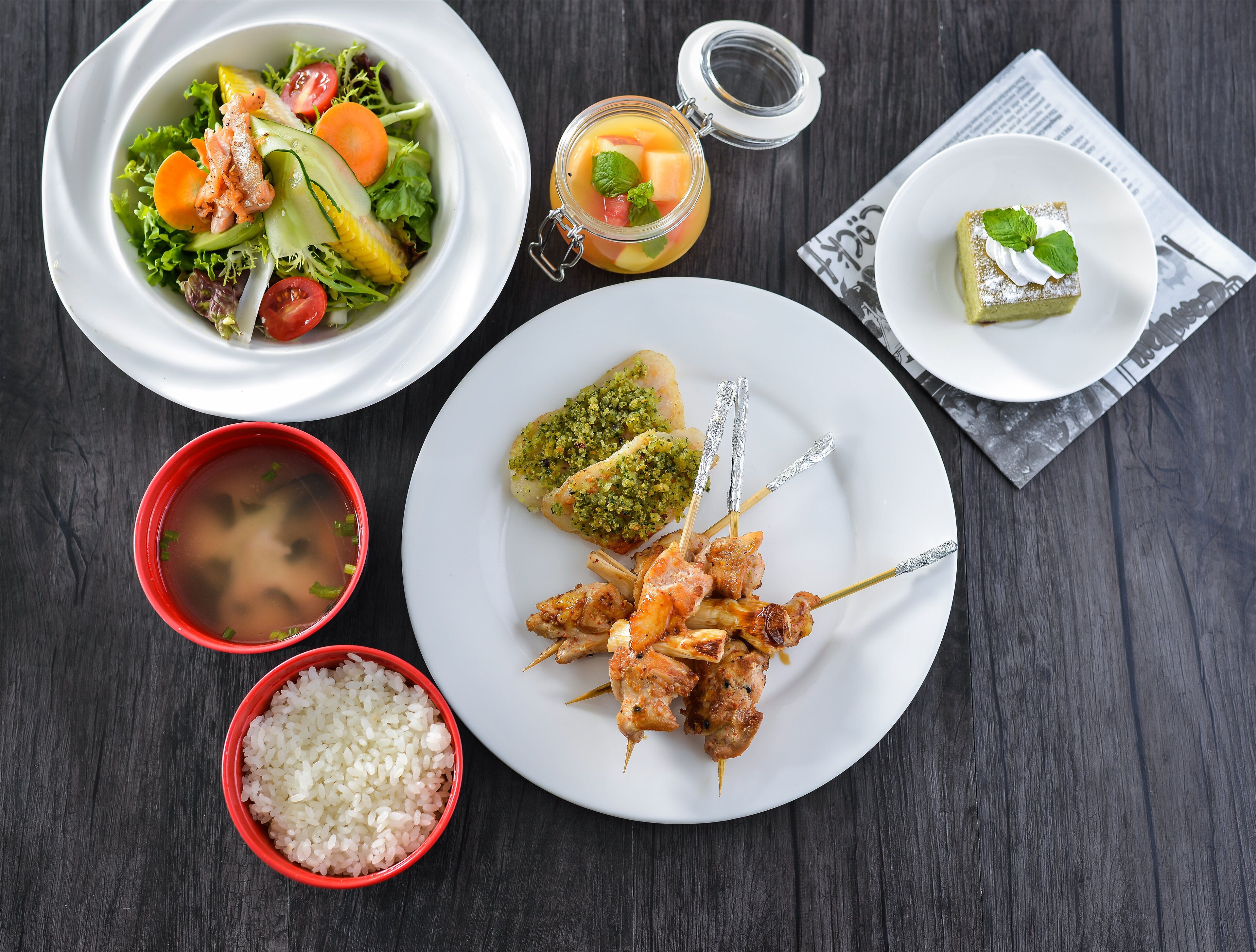 A table with a variety of dishes including a salad, skewers, rice, and a dessert.