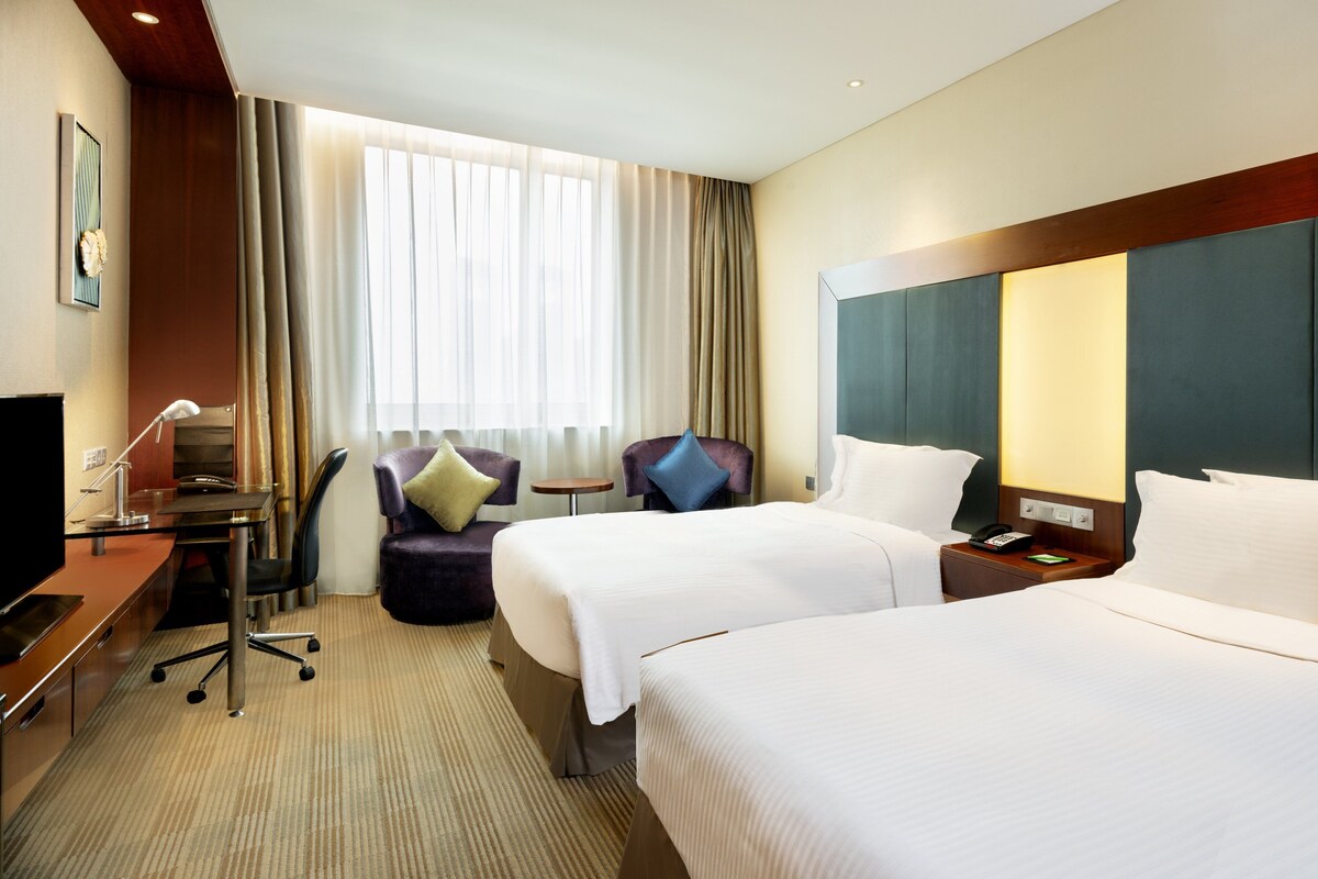 A hotel room with two beds, a desk with a computer, a chair, a small table, and a lamp.