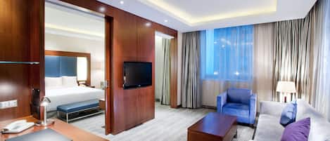 Una habitación de hotel con una cama, televisión, escritorio con teléfono, silla, sofá y mesa de centro.