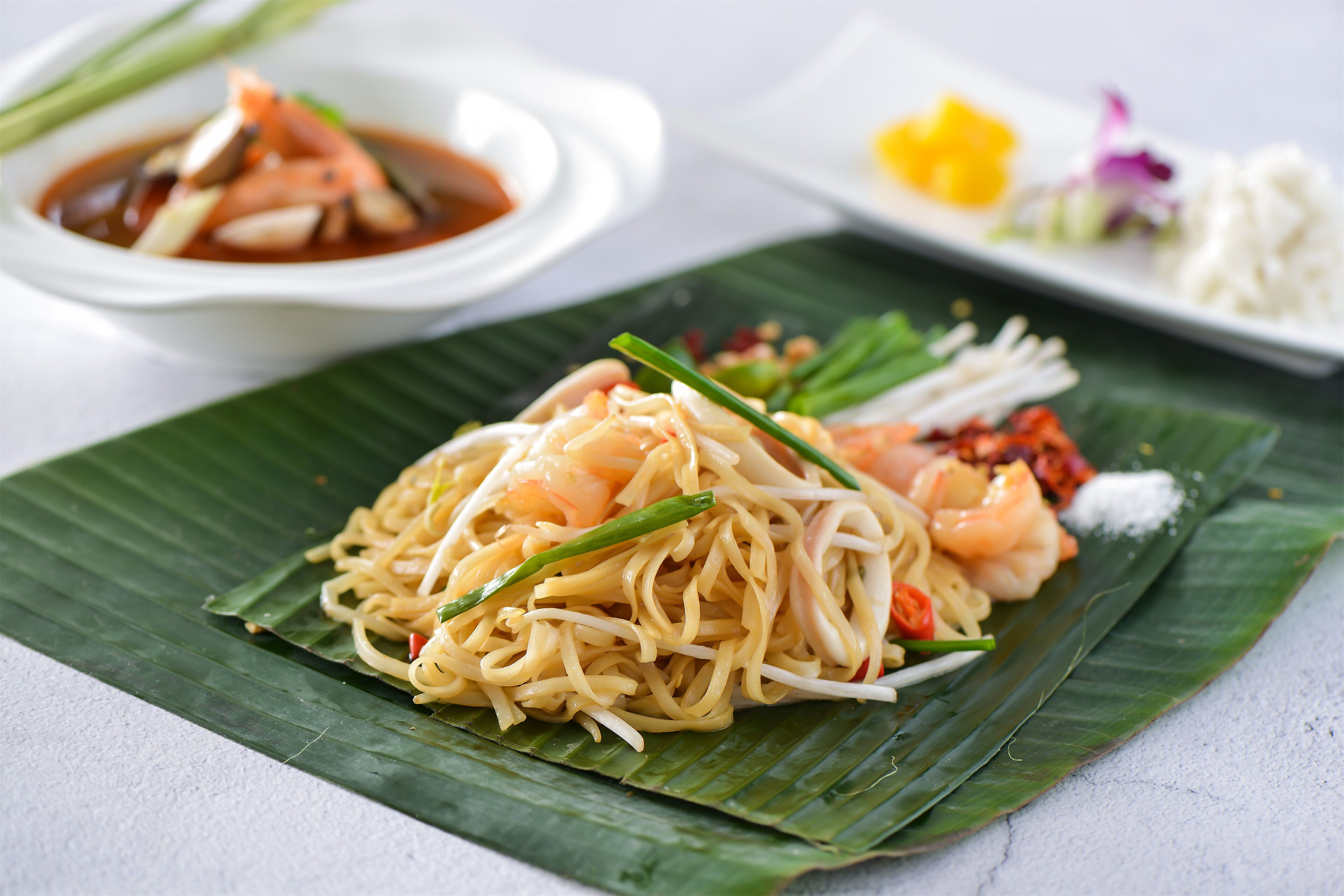 A plate of noodles with shrimp and vegetables on a banana leaf.