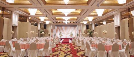A banquet hall with rows of tables, chairs, and a stage with draped curtains.