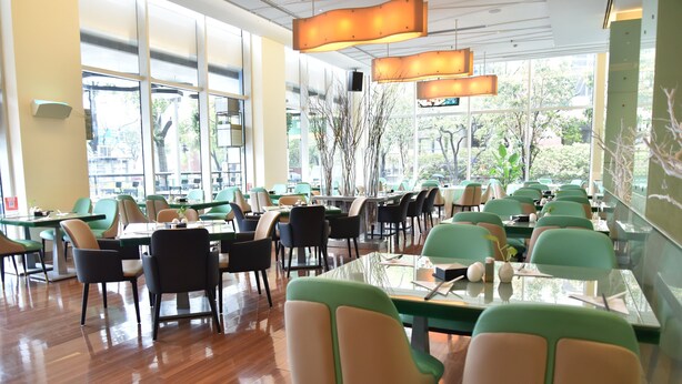 Un vaste espace de restauration intérieur, doté de nombreuses tables et chaises, de grandes fenêtres et d’un design de plafond moderne.