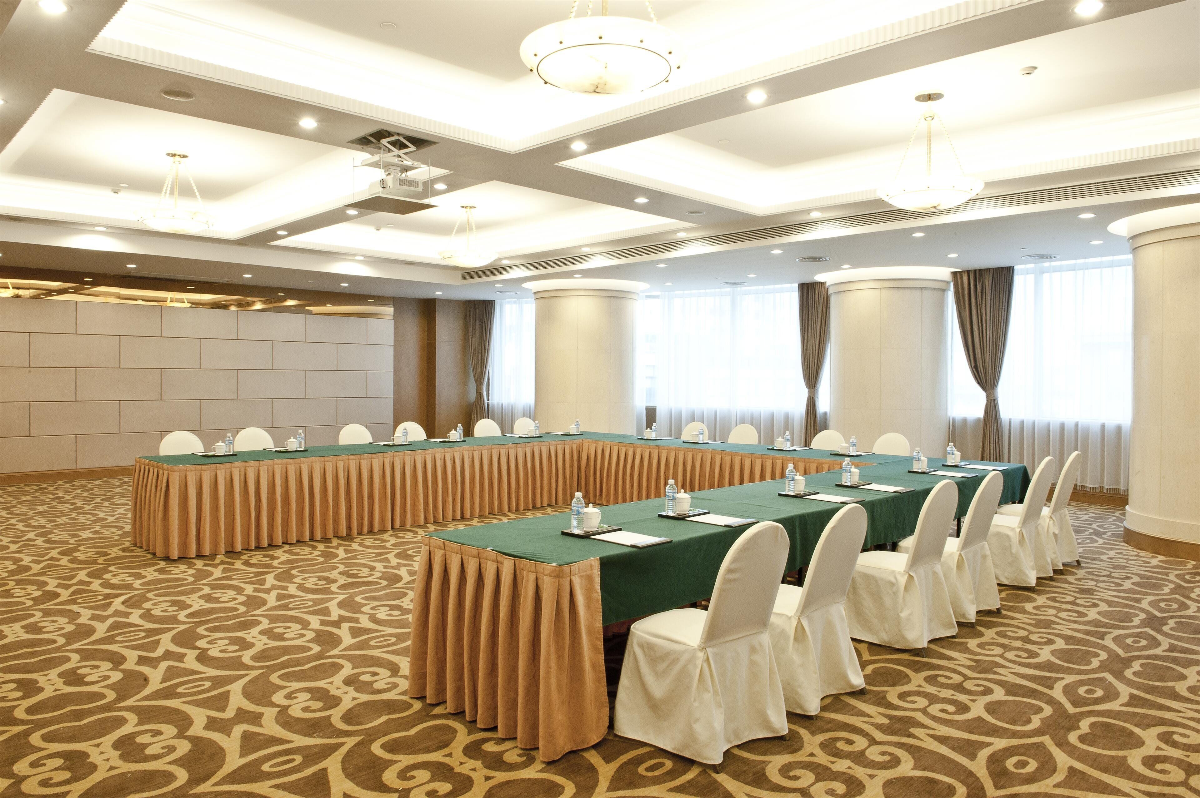 Une salle de conférence avec une longue table, des chaises blanches et un tapis à motifs.