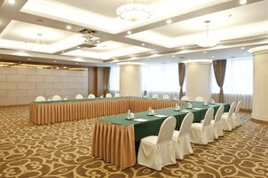 Un salón de conferencias con una larga mesa, sillas blancas y una alfombra estampada.