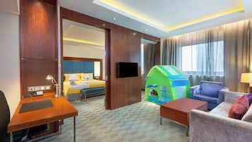 Habitación de hotel con escritorio, cama, televisor, tienda de campaña infantil y sofá.