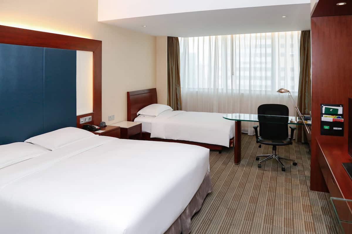 A hotel room with two beds, a desk, a chair, and a large window with curtains.