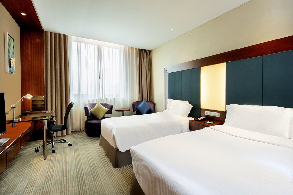 A hotel room with two beds, a desk, a chair, a small table, and a window with curtains.
