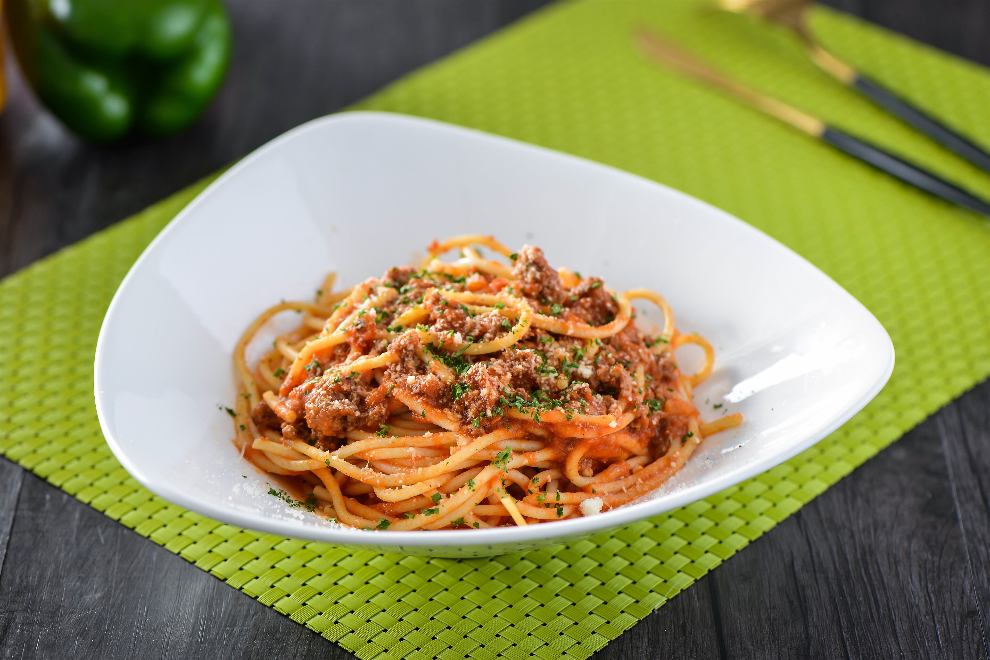 Eine weiße Schüssel Spaghetti mit Fleischsoße auf einer grünen Tischmatte.