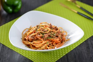 Eine weiße Schüssel Spaghetti mit Fleischsoße auf einer grünen Tischmatte.