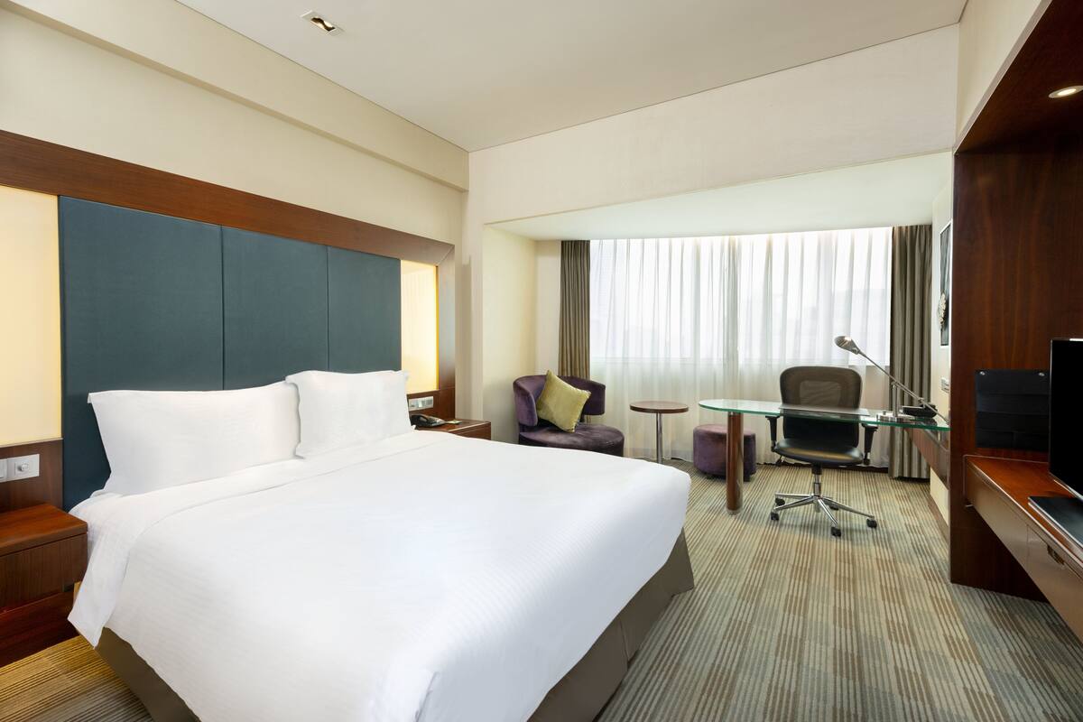 A hotel room with a large bed, a desk, a chair, and a TV.