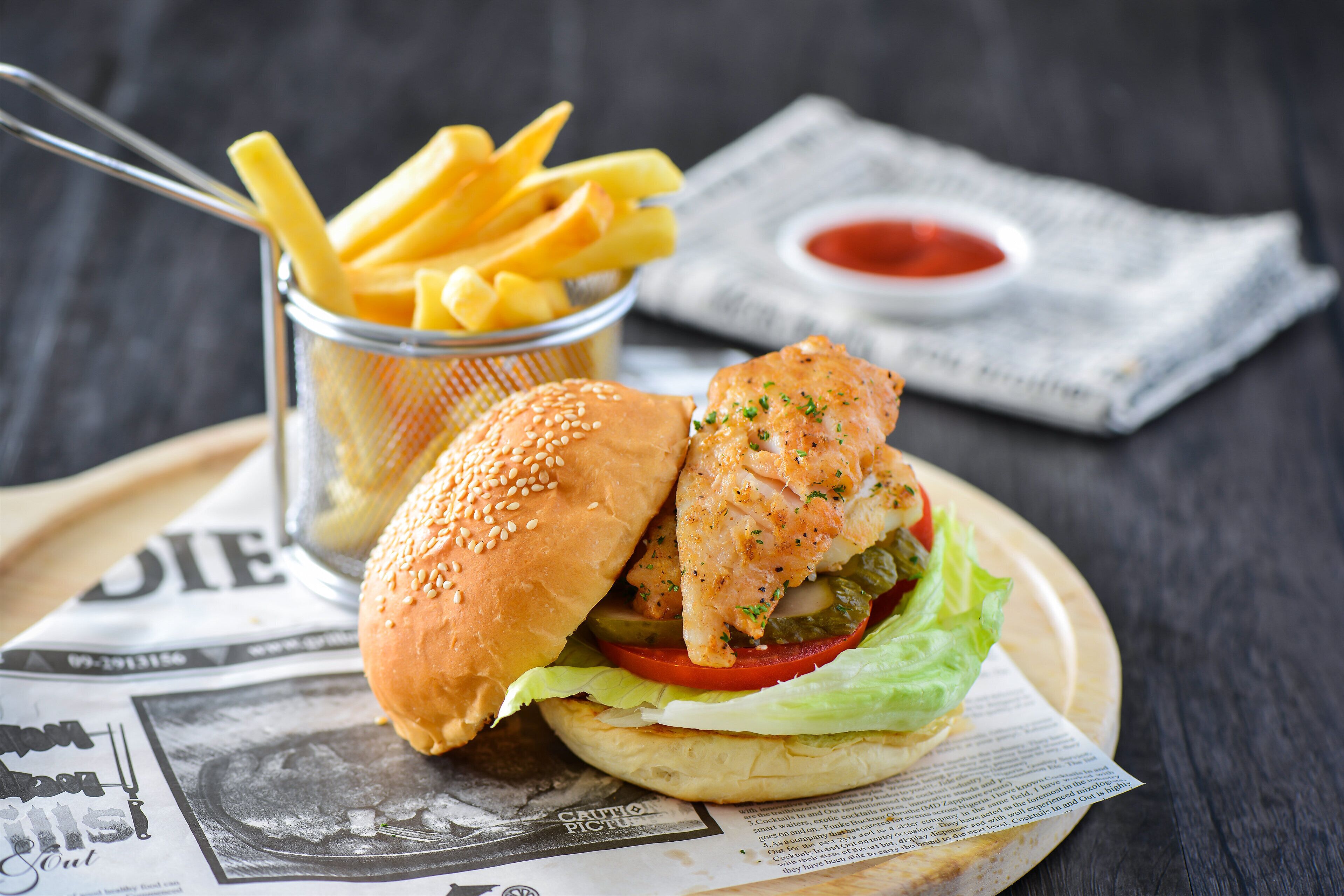 Una hamburguesa con papas fritas y kétchup sobre un periódico.