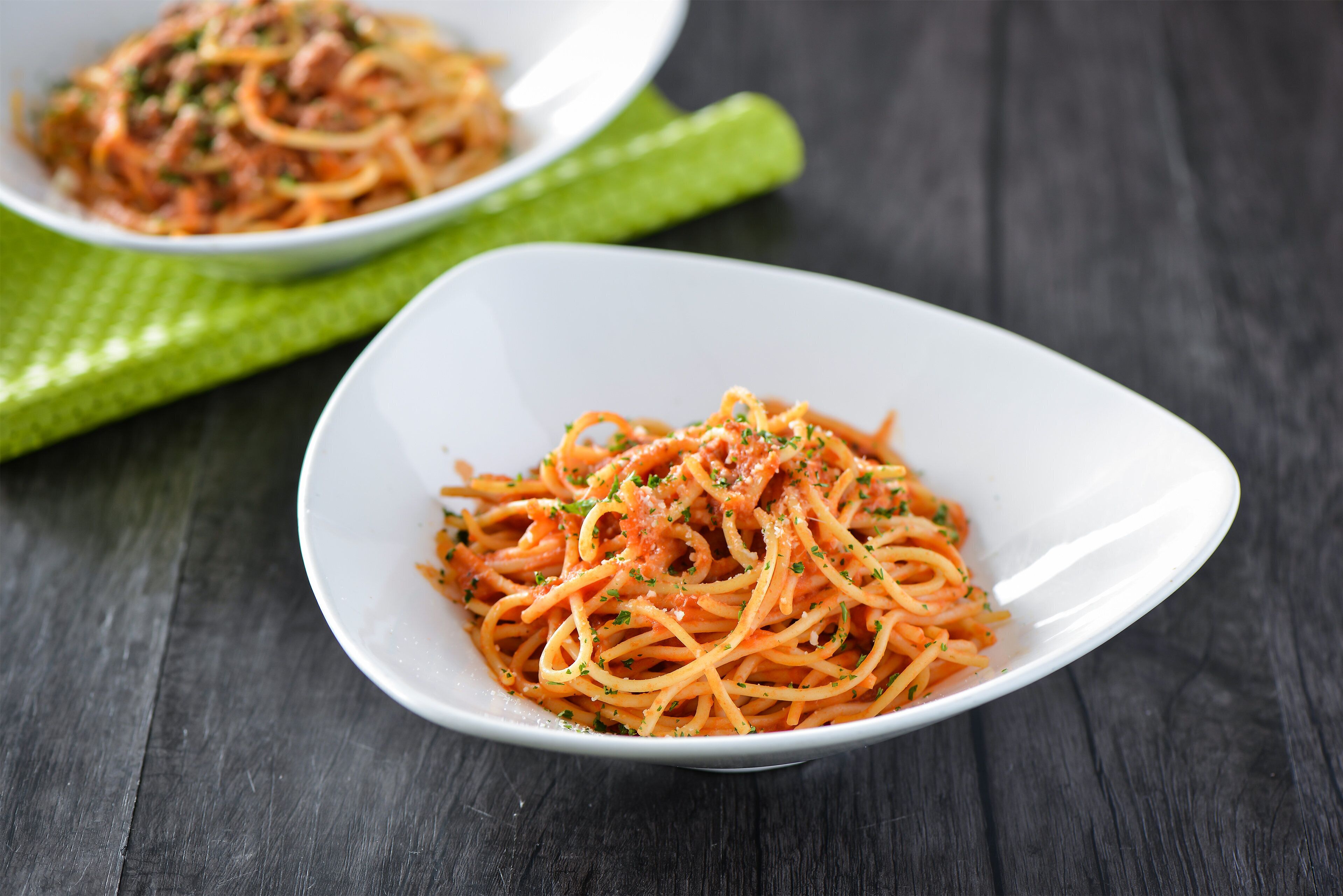 A white plate of spaghetti with a red sauce, garnished with herbs, on a dark wooden table.