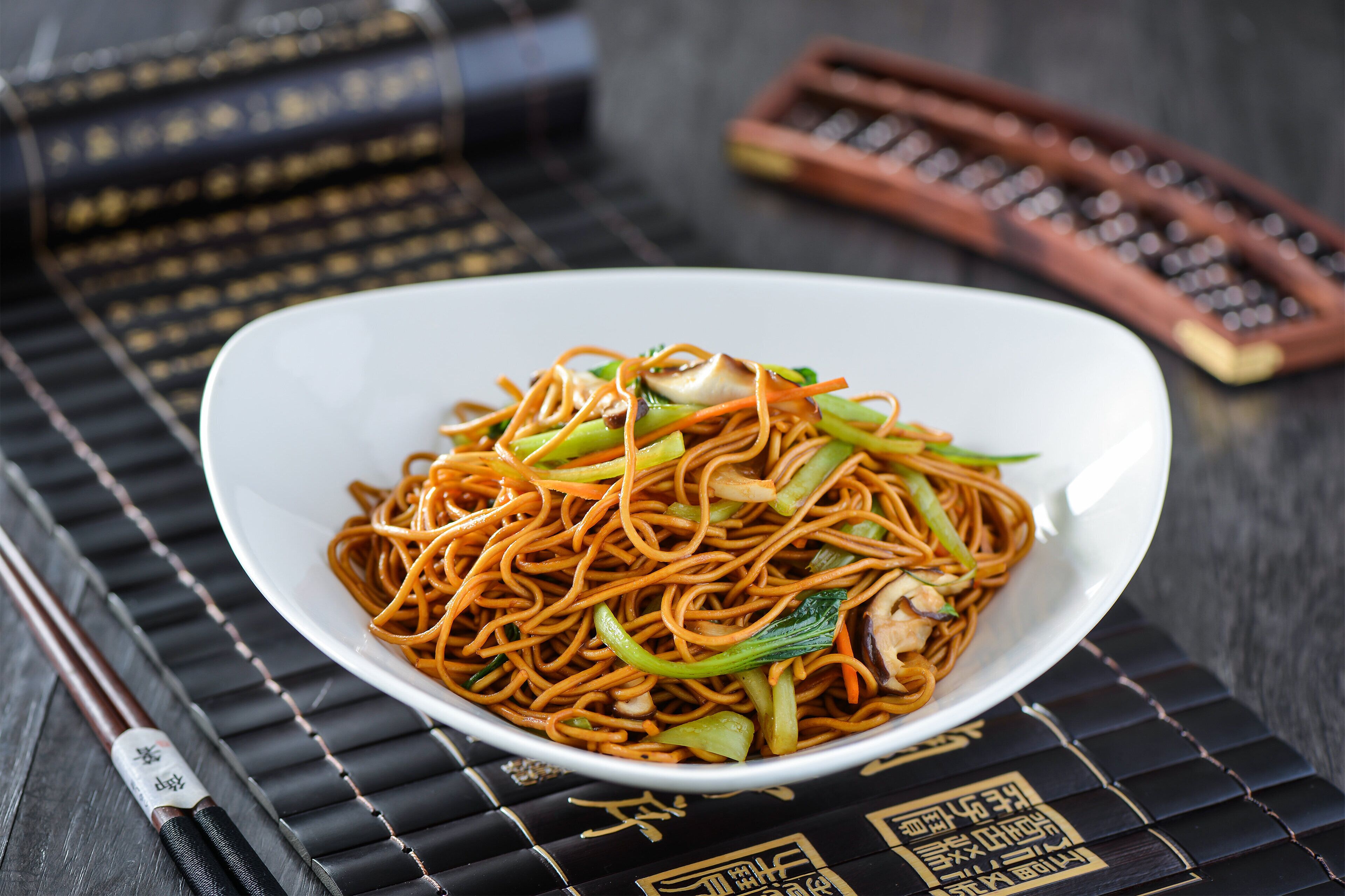 A bowl of noodles with vegetables on a black mat with gold patterns.