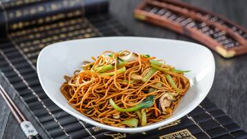 A bowl of noodles with vegetables on a black mat with gold patterns.