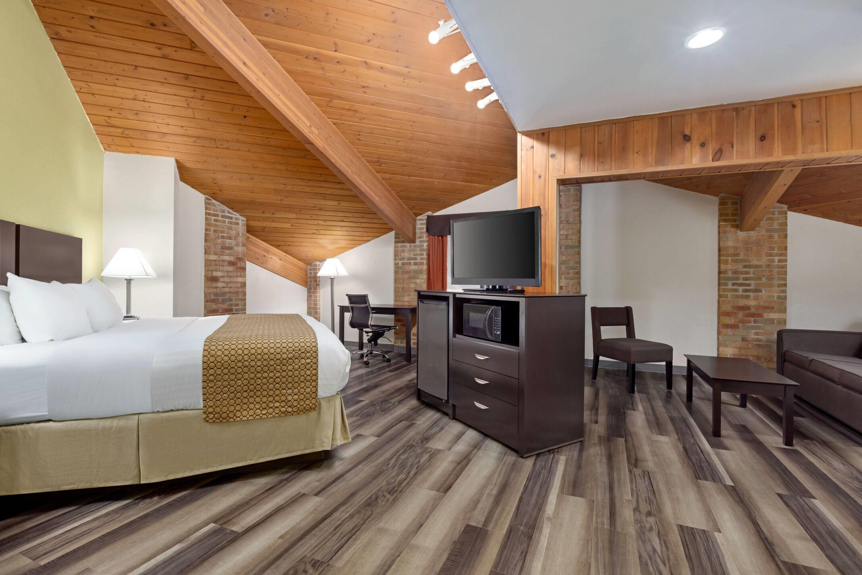 A hotel room with a bed, desk, TV, and seating area.