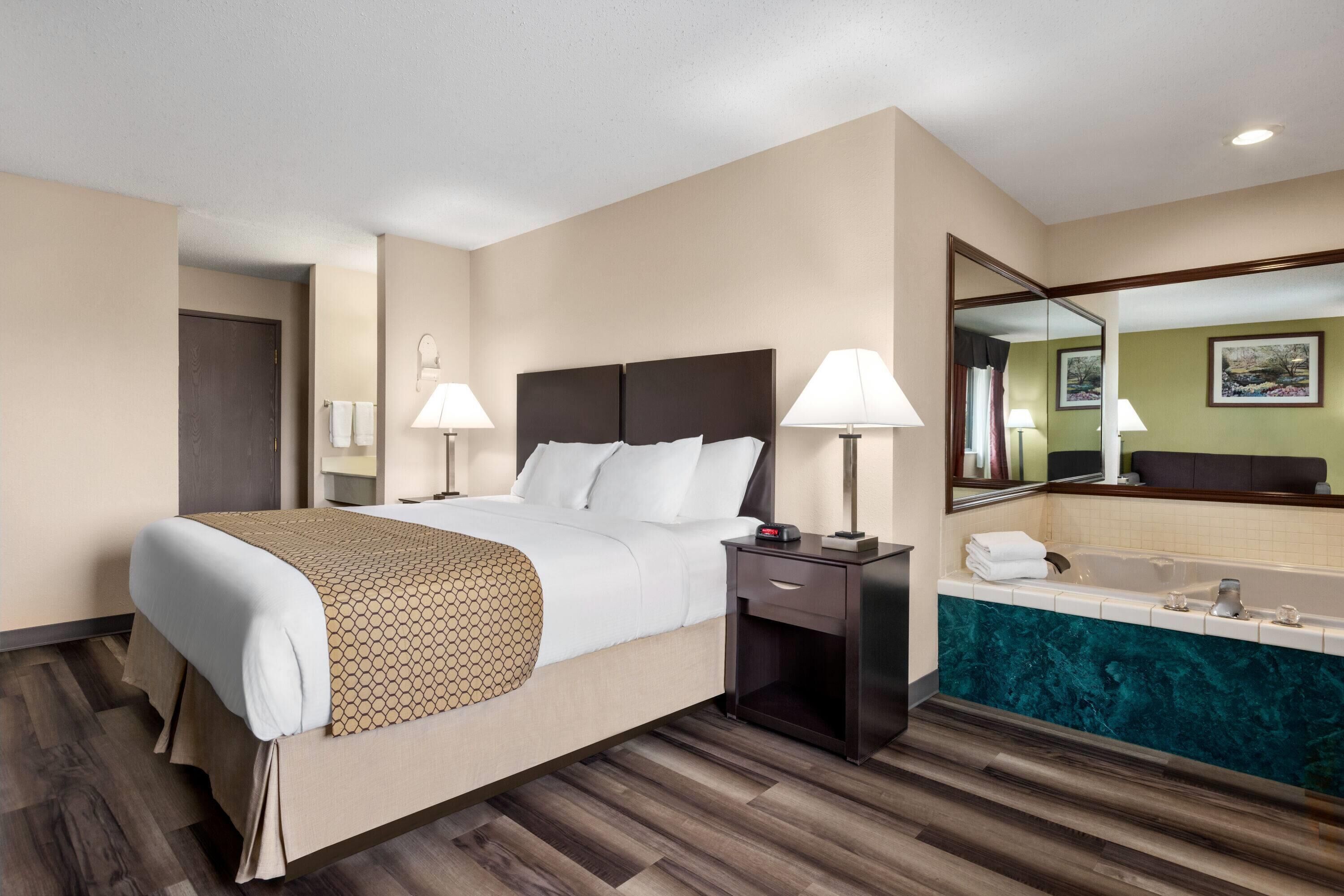 Habitación de hotel con una cama grande, lámparas de noche, mesita de noche, baño con bañera y espejo.
