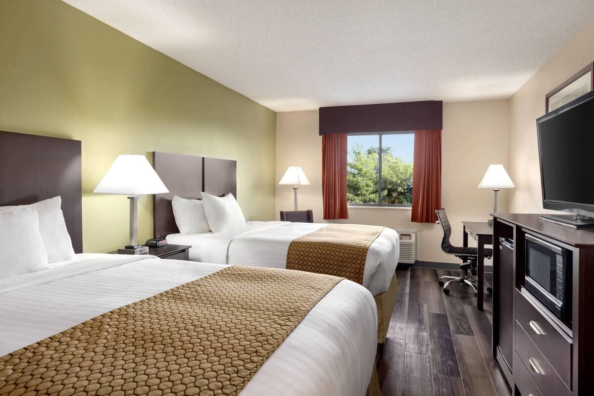 A hotel room with two beds, a desk, a TV, and a window with curtains.