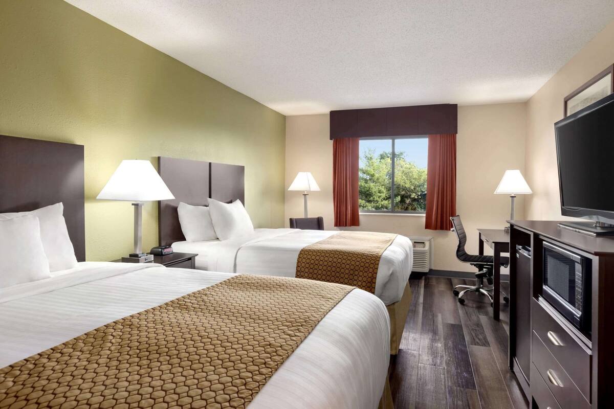 A hotel room with two beds, a desk, a TV, and a window with curtains.