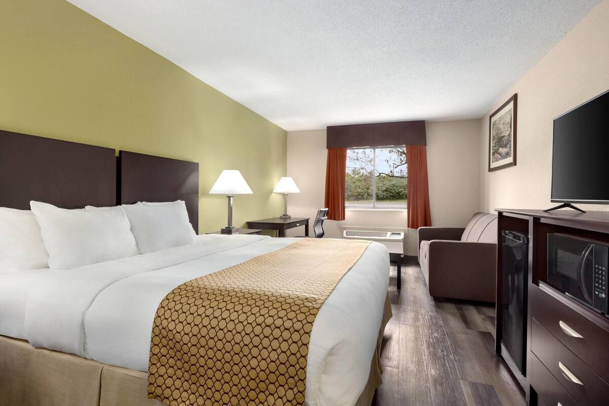 A hotel room with a large bed, a desk, a chair, a television, and a microwave.