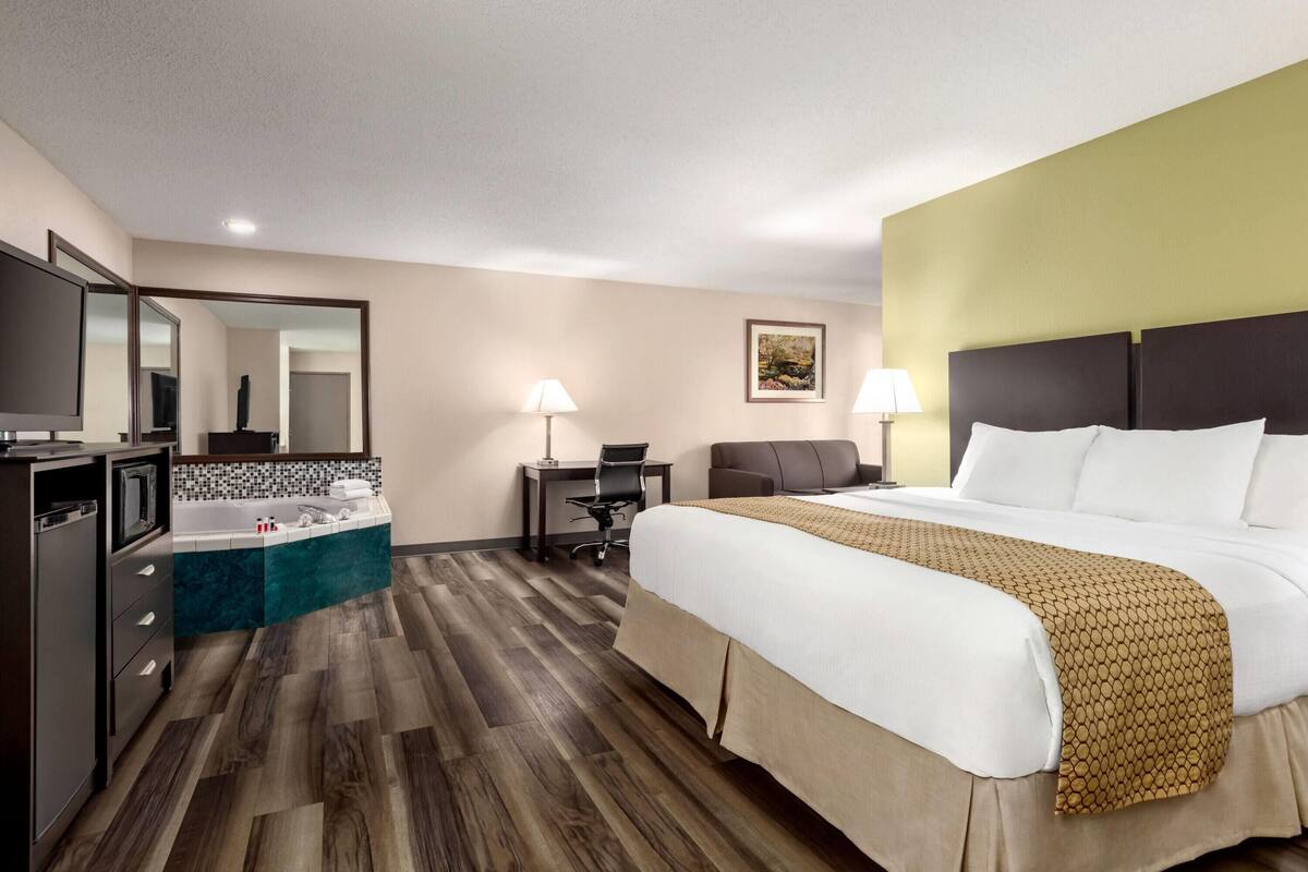A hotel room with a large bed, a desk, a chair, a TV, a bathroom with a bathtub, and a mirror.