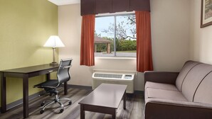 A hotel room with a desk, chair, sofa, and a window with curtains. - Baymont by Wyndham Monroe (Monroe)